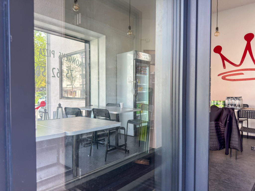 Enkel indretning hos Kongens Pizza & Grill med få borded og stole i det lille fastfoodsted.